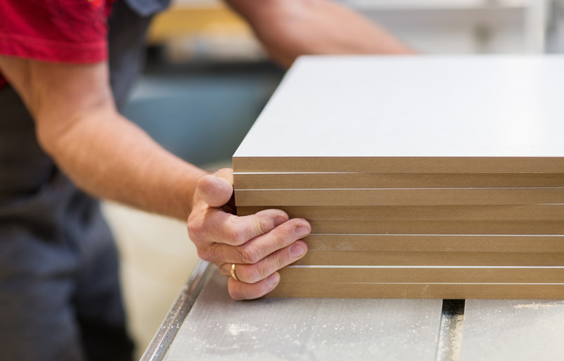 Close up of a carpenter with a stack of MDF boards in a workshop