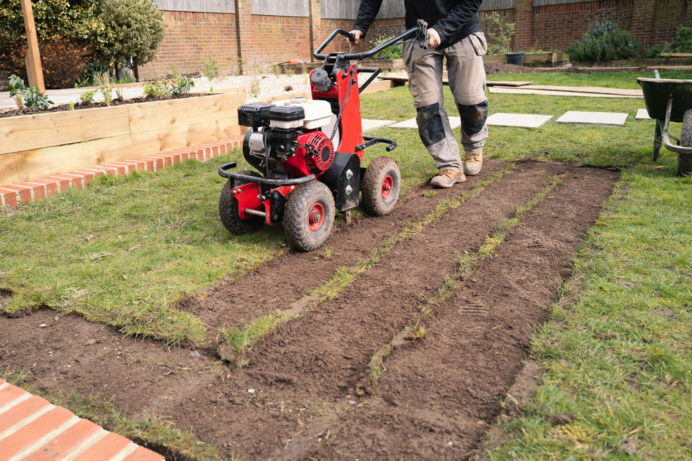 A gardener uses a turf cutter to prepare the ground for artificial grass.