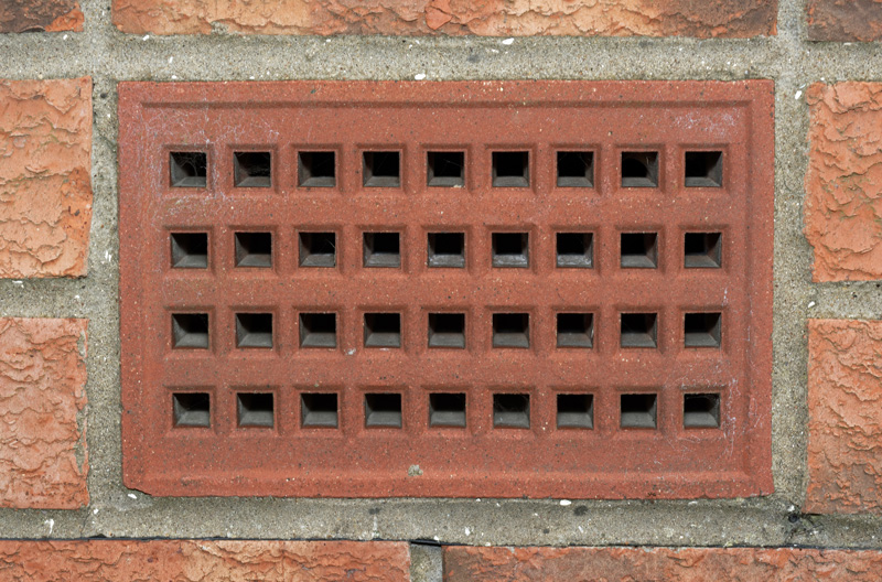 an air brick surrounded by regular bricks in the exterior wall of a building 