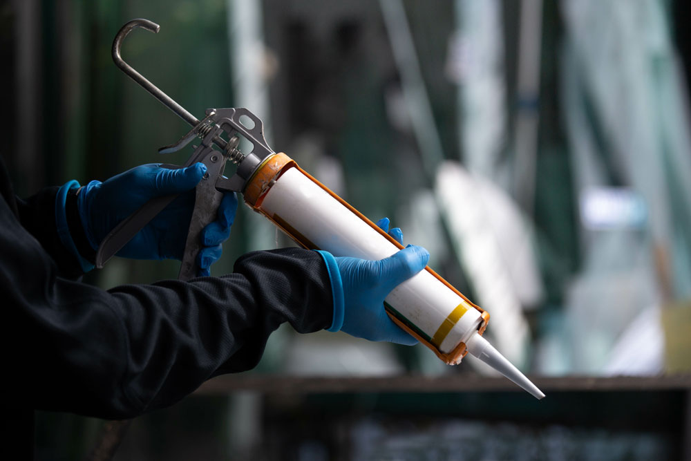 A construction worker holds a tube of sealant in a sealant applicator gun.