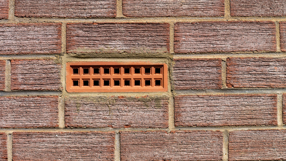 an air brick embedded in a textured red brick exterior wall