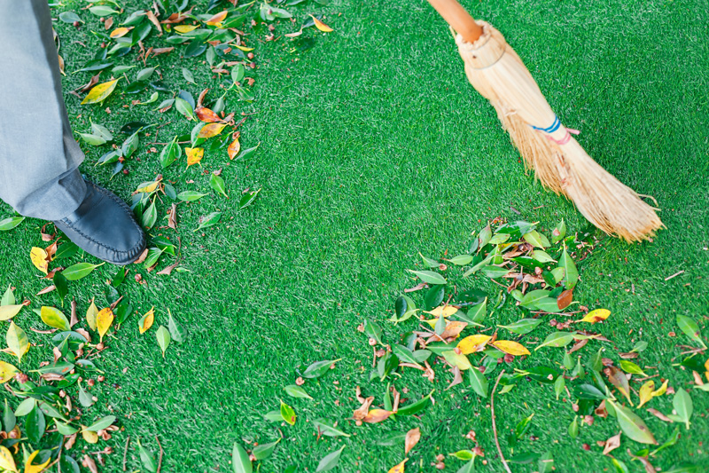  A person brushes dead leaves off their artificial lawn using a soft-bristled broom.