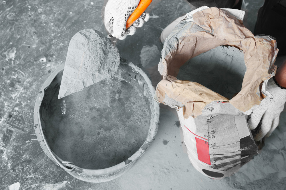 a worker with cement powder and a trowel mixing concrete in a bucket