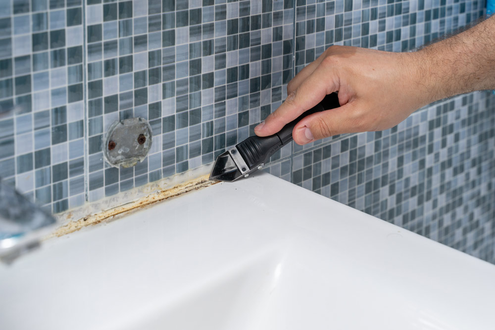 A man removing dirty silicone sealant in a bathroom. 